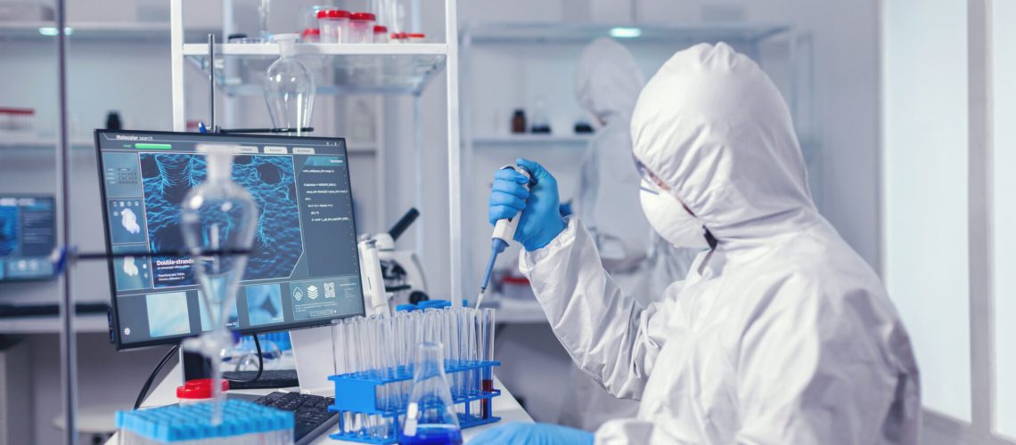 Engineer in microbiology lab holding micropipette with sample from test tube. Chemist in modern laboratory doing research using dispenser during global epidemic with covid-19.